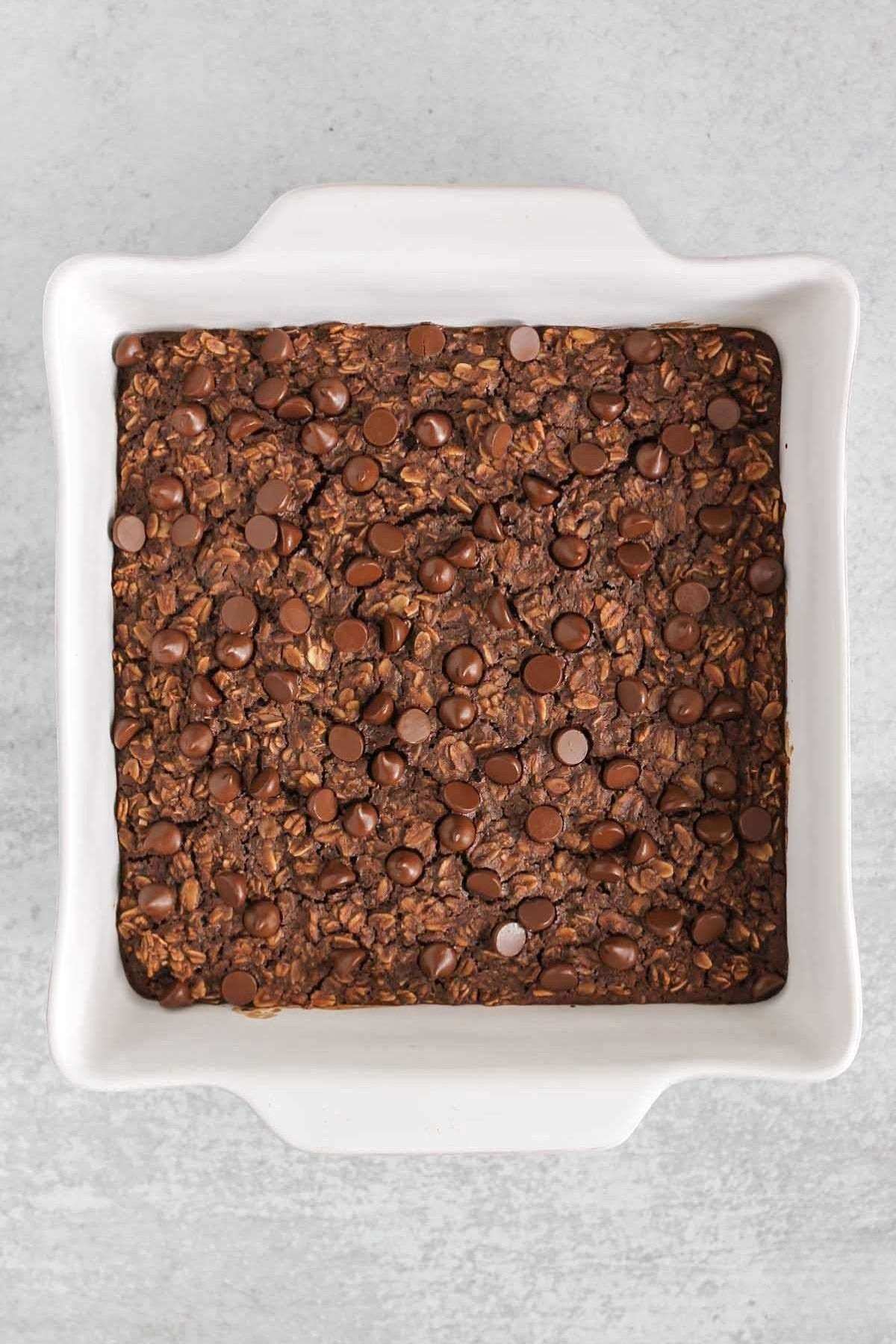 Chocolate baked oats topped with chocolate chips is a square baking dish.