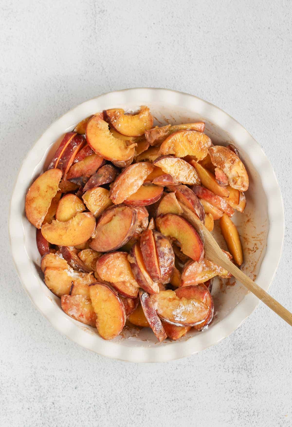 Slice fresh peaches in a ceramic pie dish mixed with cinnamon and tapioca starch.