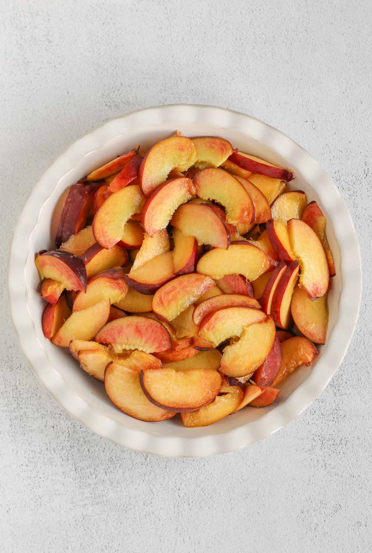 Sliced peaches in a ceramic pie plate.