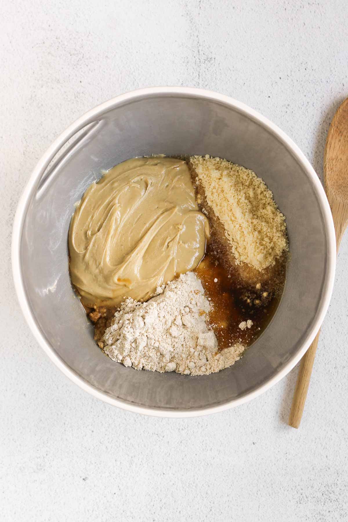 Ingredients for protein ball dough, unmixed, in a large mixing bowl with a wooden spoon on the side.