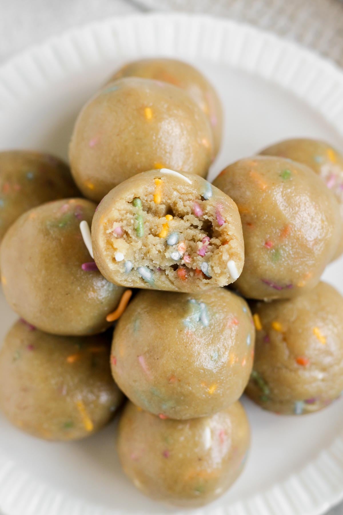 Birthday cake protein balls stacked on a round plate with a bite taken from the top ball.
