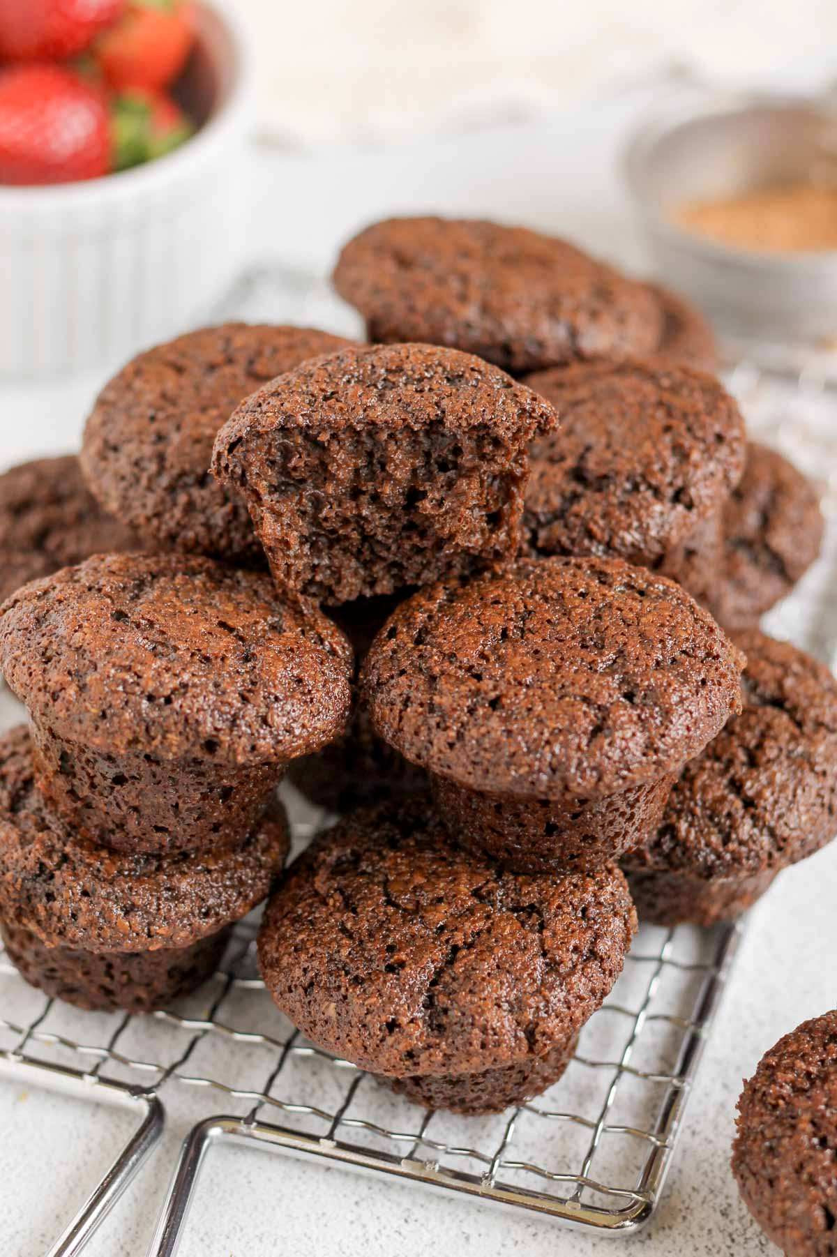 Mini chocolate flaxseed muffins stacked on a cooling rack with the top one split in half to show texture.