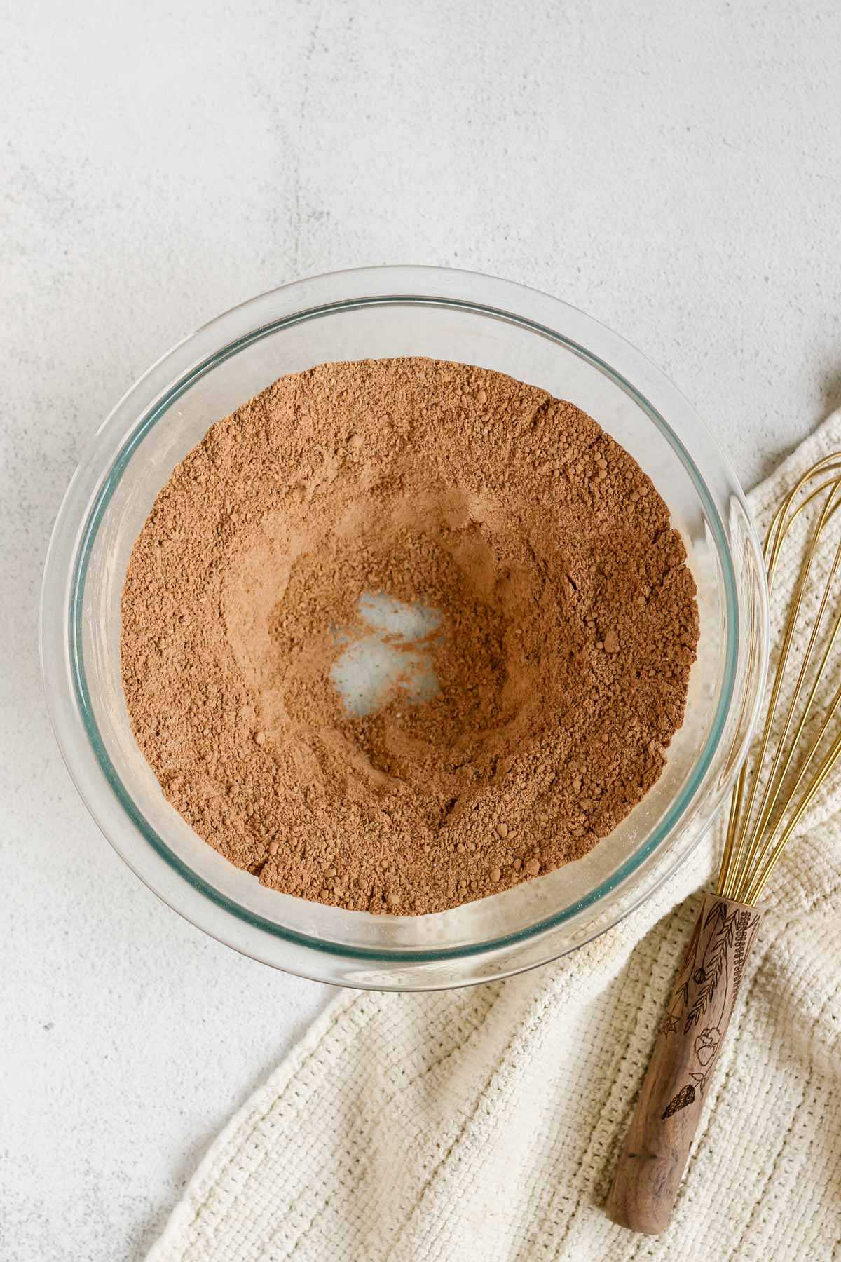 Dry ingredients for chocolate flaxseed muffins in a glass mixing bowl with a well in the center of the ingredients.