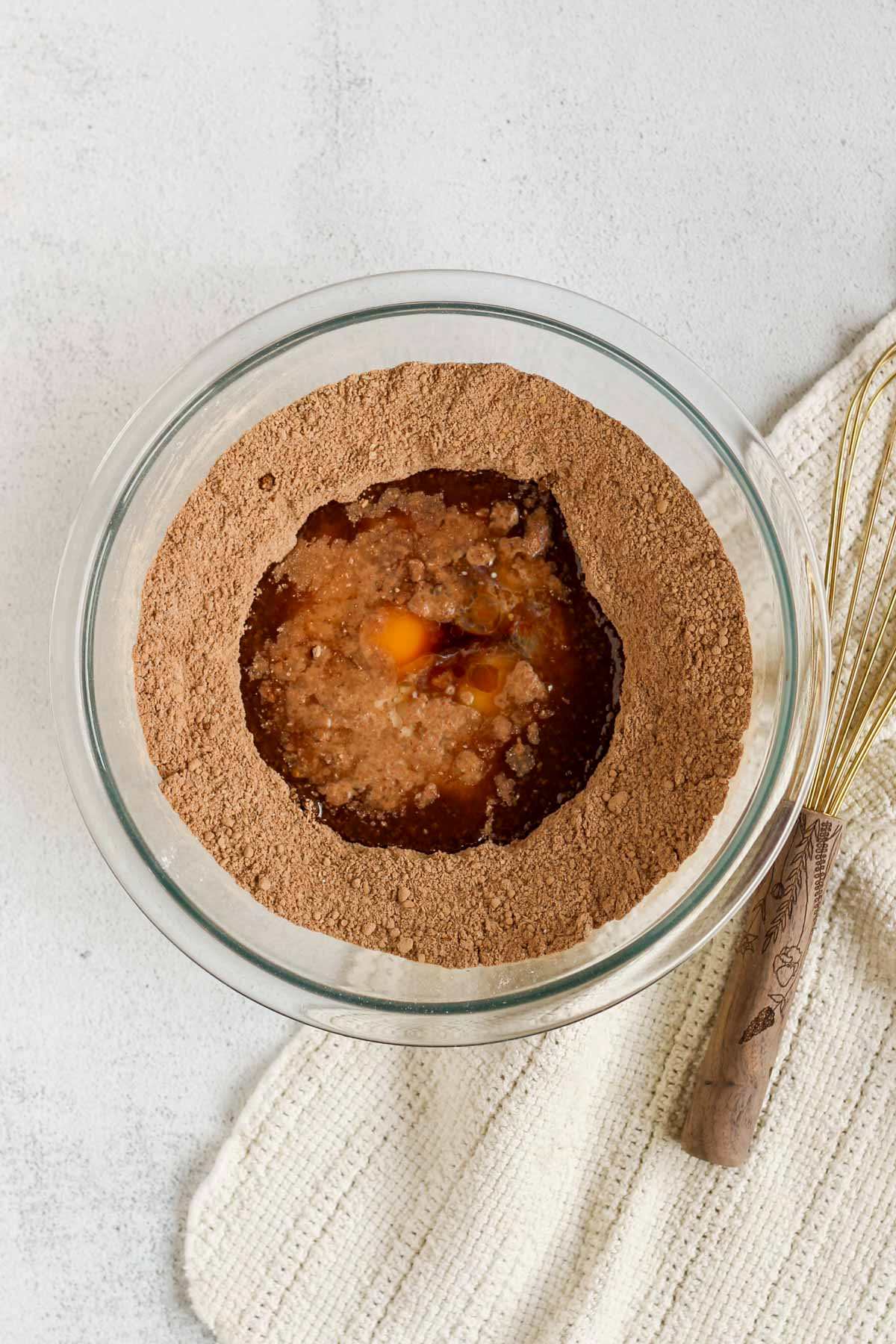Chocolate muffin dry ingredients in a glass mixing bowl with a well in the center filled with wet ingredients.
