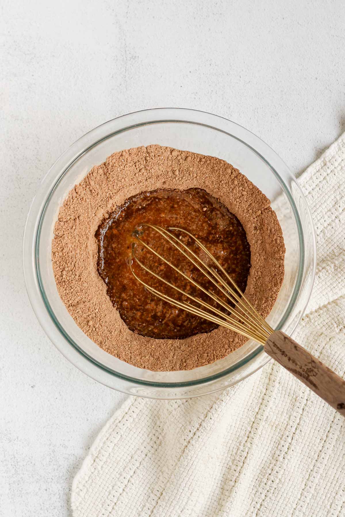 Glass mixing bowl with dry ingredients and a well inside with wet ingredients whisked together with a whisk in the bowl.