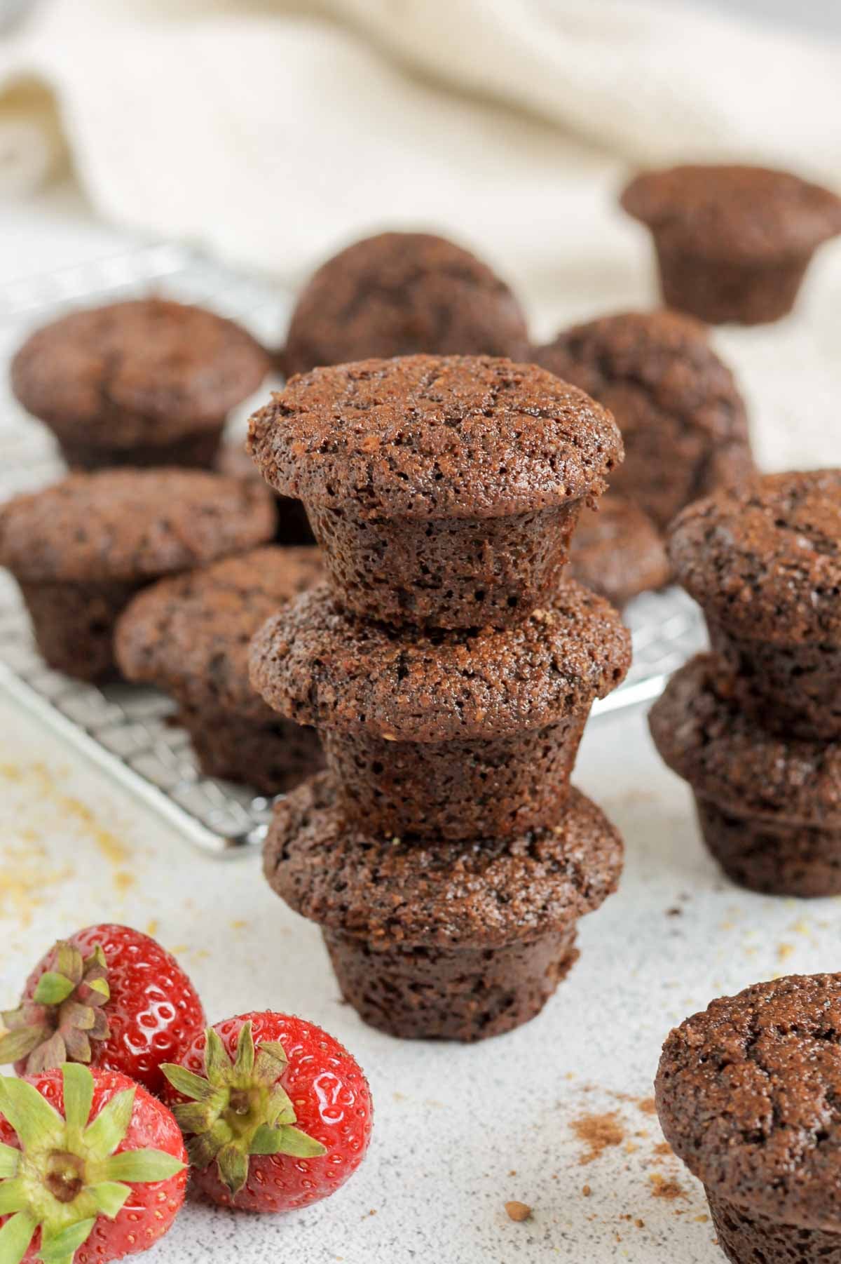 Three chocolate mini muffins stacked on top of each other with additional muffins in the background.