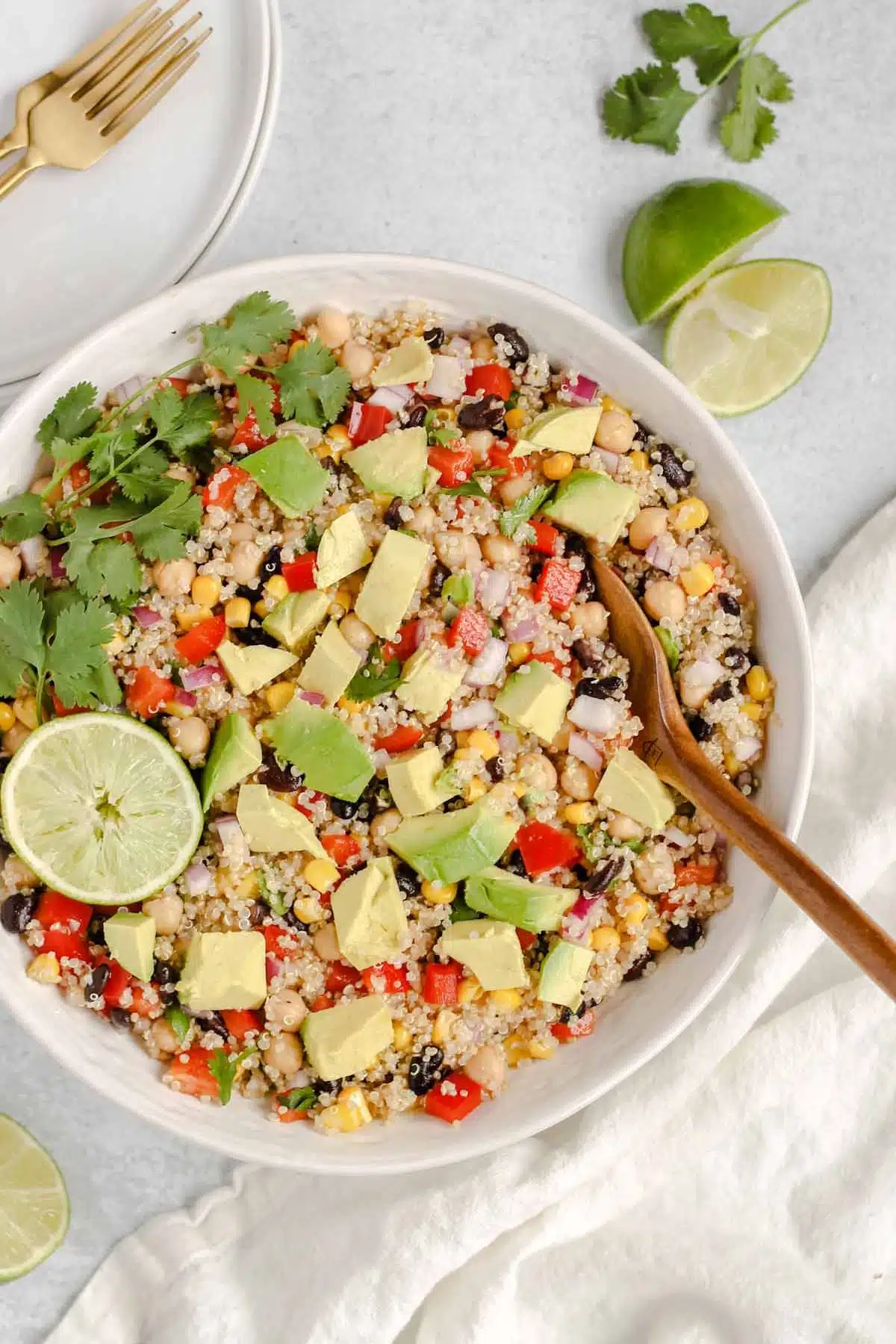Southwest quinoa salad topped with avocado pieces, fresh cilantro and a lime wedge in a large serving bowl.