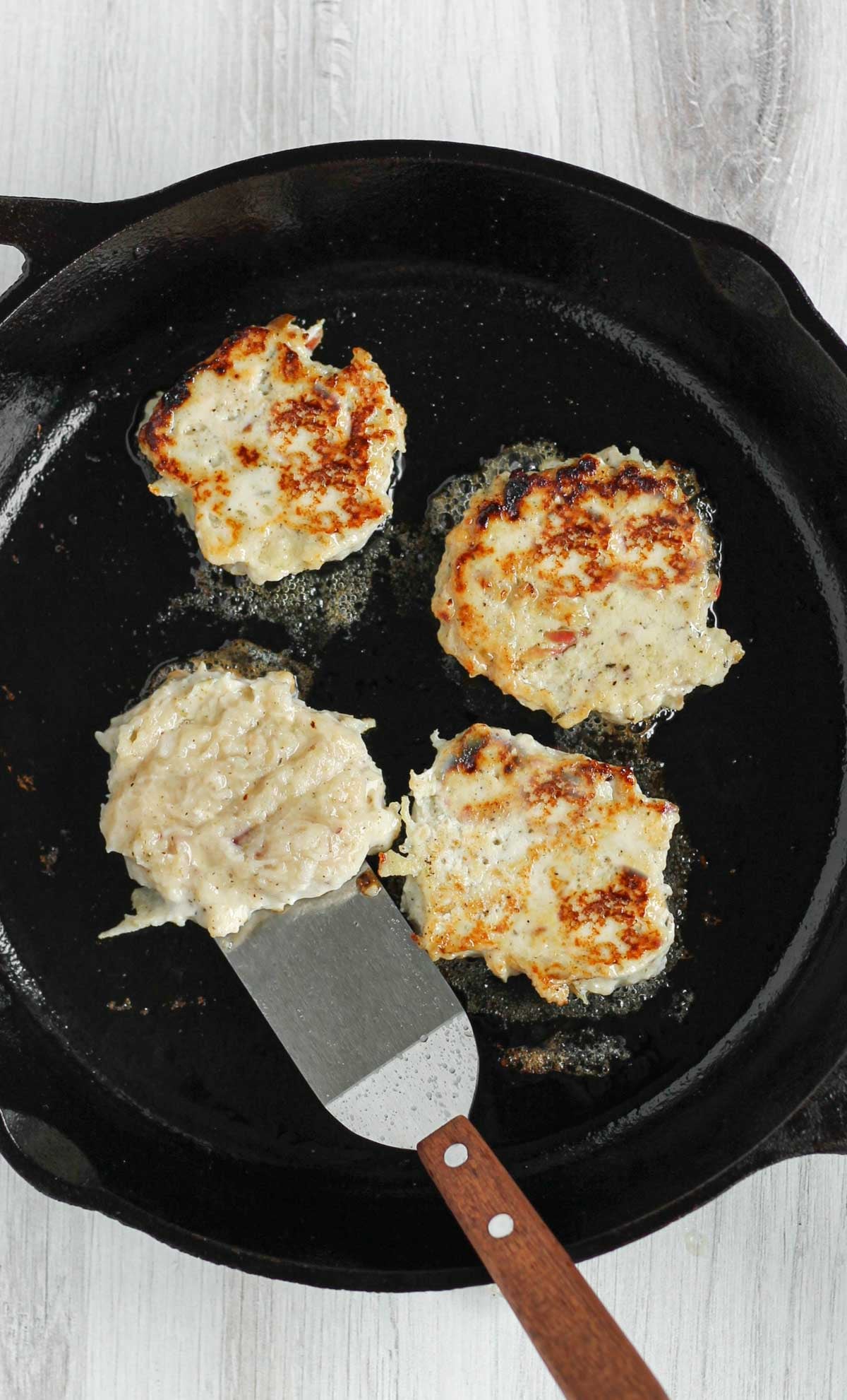 Stainless steel spatula flipping a chicken sausage patty in a cast iron skillet.