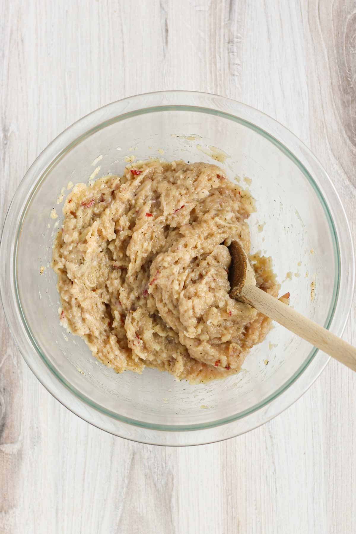 Ground chicken mixed with apples and chicken sausage seasoning in a glass bowl with a wooden spoon in the bowl.