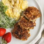 A plate with 3 chicken sausage patties, scrambled eggs, greens, and strawberries.