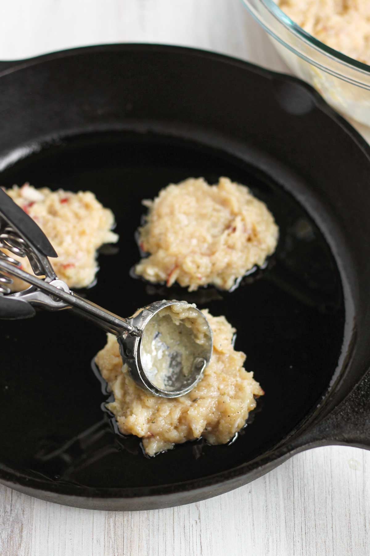 Spring loaded scoop pushing a raw sausage patty onto a cast iron skillet.