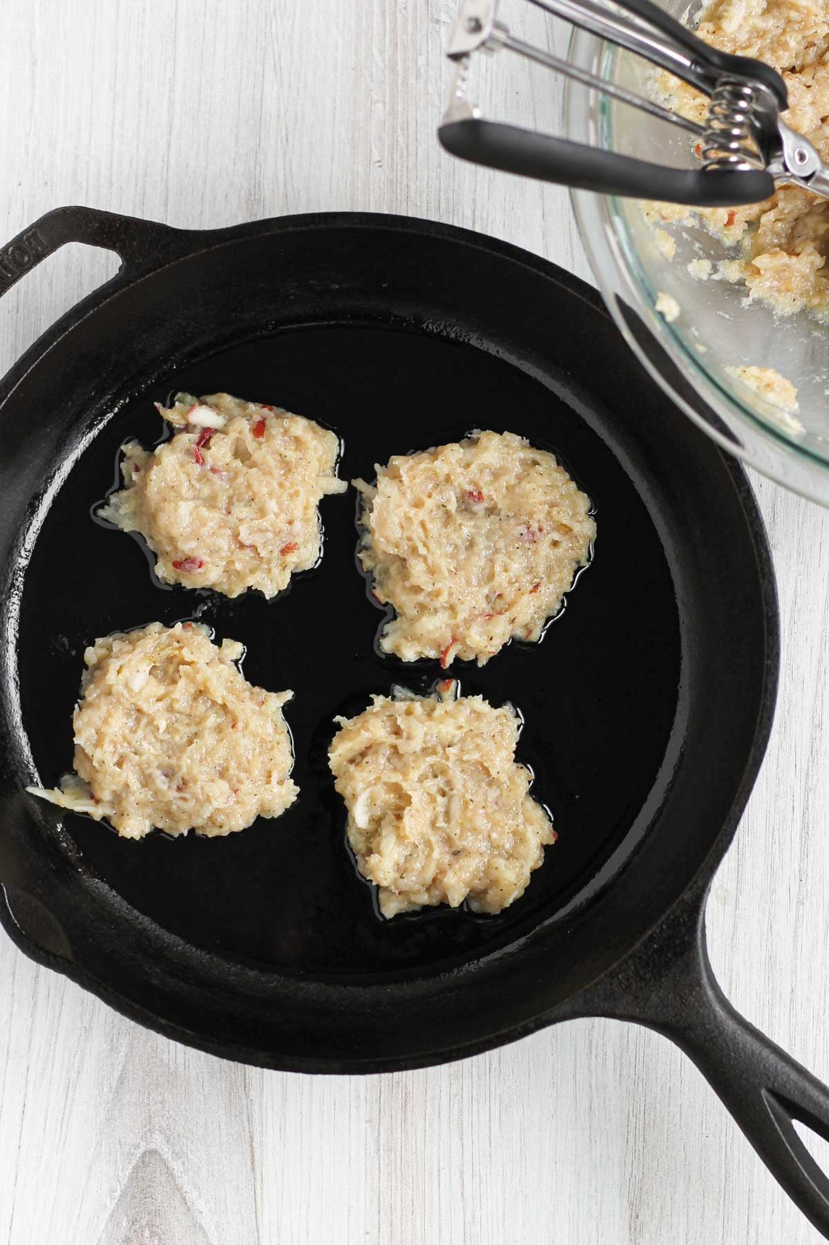 Four ground chicken breakfast sausage patties cooking in a cast iron skillet.