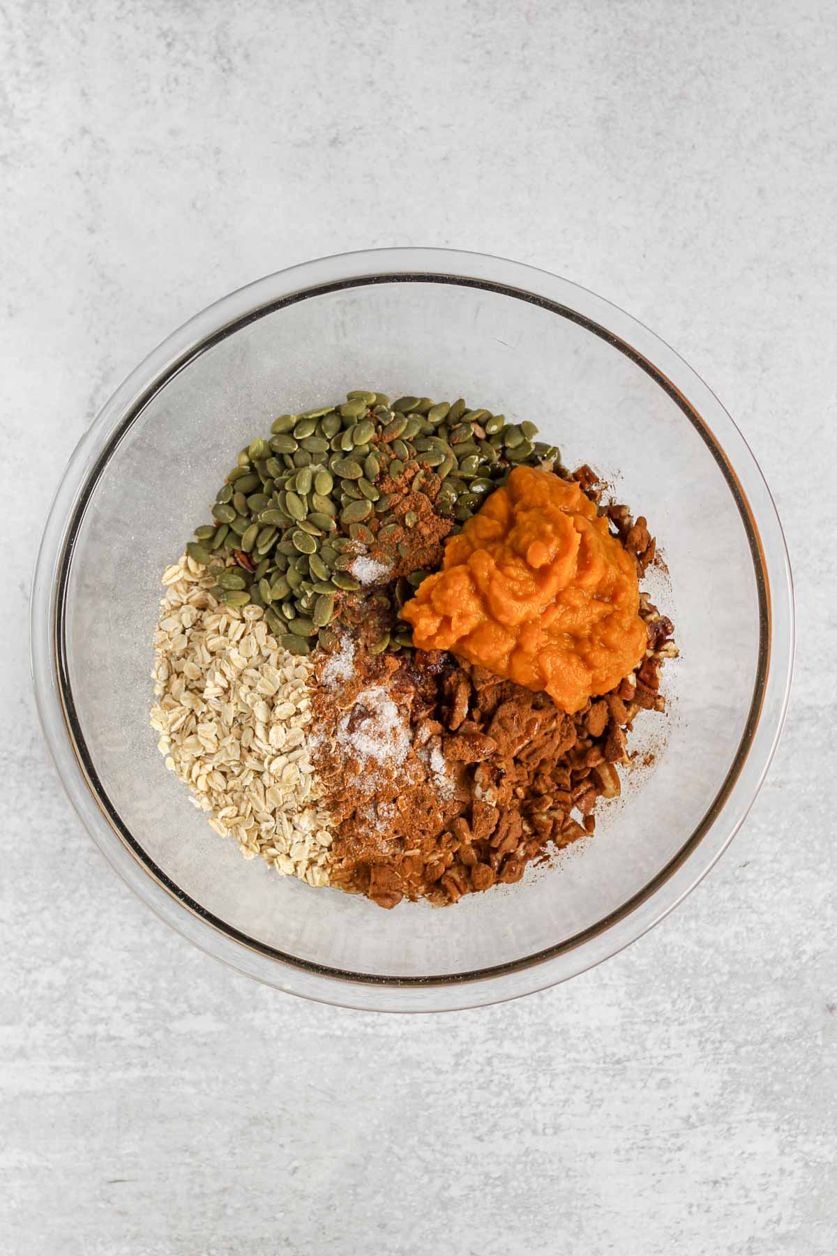 Ingredients for pumpkin granola in a large glass mixing bowl before being mixed together.