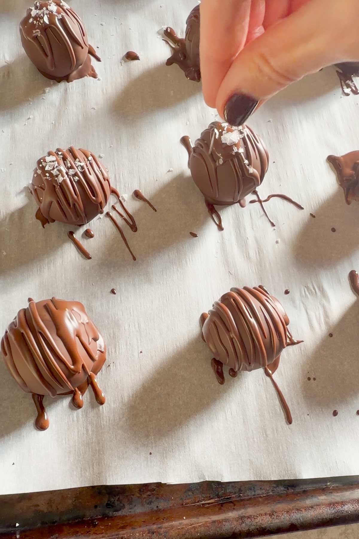 Flaky sea salt being sprinkled over chocolate covered pumpkin truffles.
