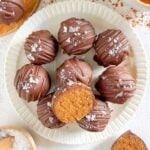 Pumpkin truffles on a small round plate with one truffle cut in half. Half truffle lying on the plate and other half next to the plate.