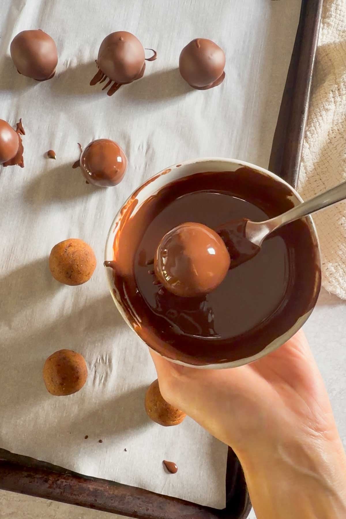 Pumpkin truffle bowl being dipped in melted chocolate.
