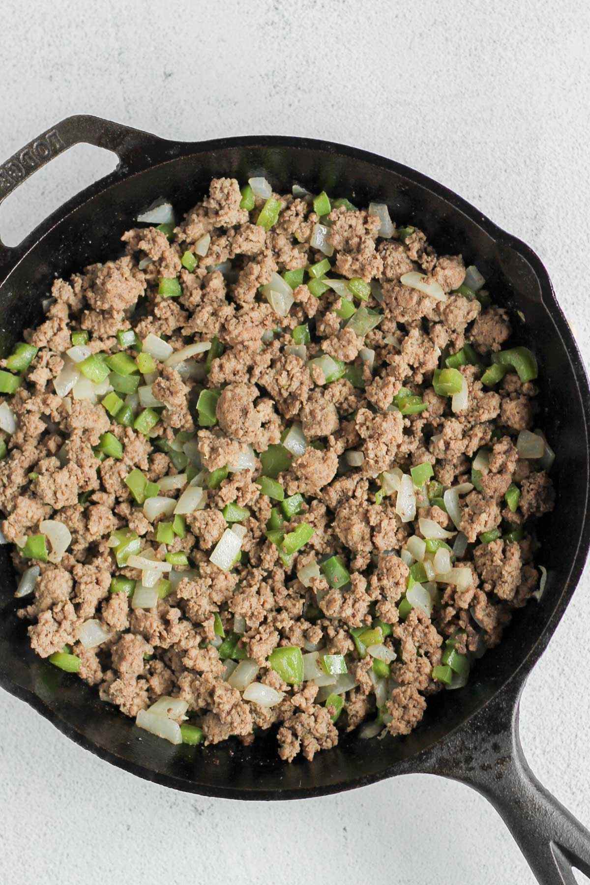 Cooked ground beef with green peppers and onions in a cast iron skillet.