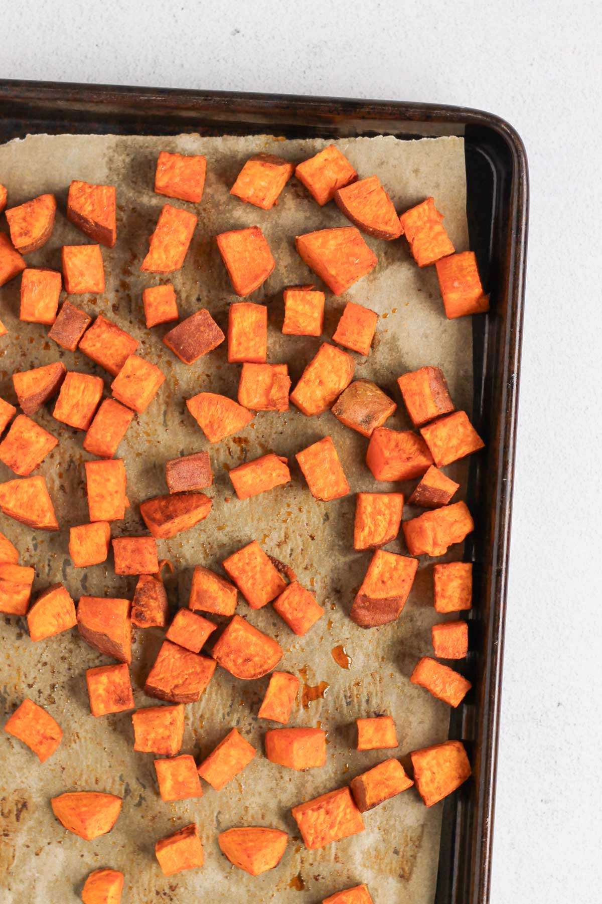 Roasted sweet potatoes on a parchment paper lined baking sheet.