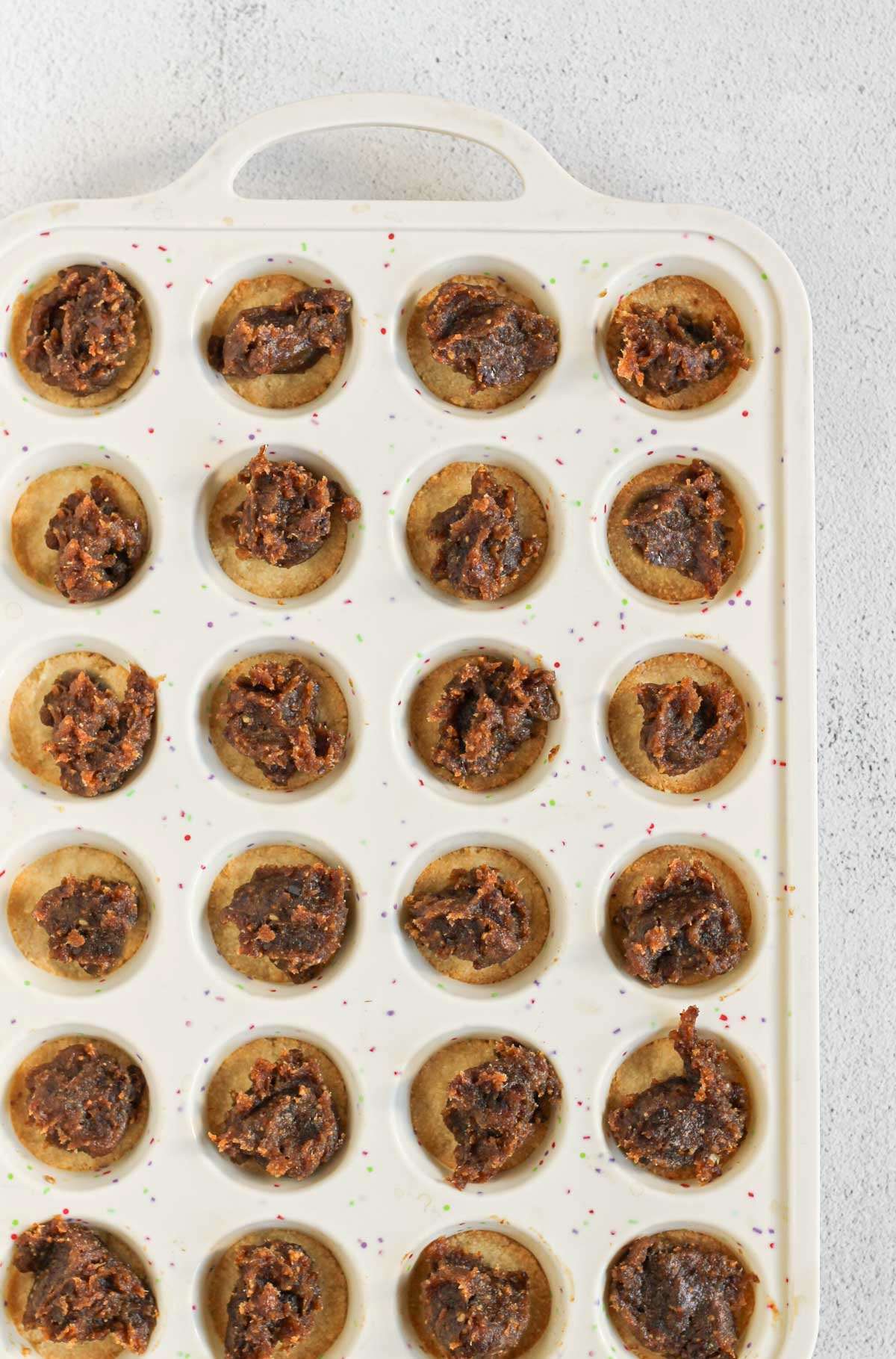 Silicone mini muffin pan with shortbread base and scoops of date caramel added to each muffin cavity.