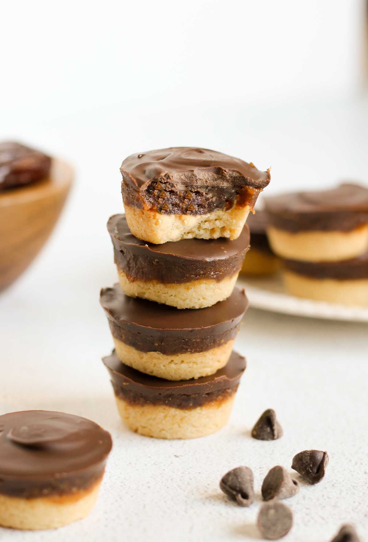 Round Twix bites stacked 4 high with a bite taken from the top one. Additional Twix bites and a bowl of dates in the background.